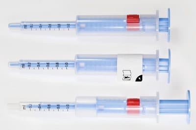 Die Dosierspritze im Originalzustand mit nicht aktiviertem Knopf (oben), mit Label zum Schutz des Knopfes (Mitte) und mit eingestellter Dosis nach Knopfaktivierung (unten)