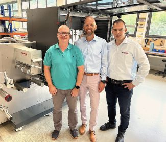 Sascha Zapf (Vertriebsleiter bei MPrint) und David van Loo (Vertriebs- und Marketingleiter bei MPrint)  zusammen mit Ahmed Türkmen (Vertriebsleiter bei Vetaphone) vor einer MLabel 3-Anlage von am Firmensitz in Baiersbronn (Quelle: The Publicity Studio)